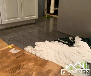Water damage restoration showing buckled hardwood flooring and remediation materials on the floor of a kitchen area with white cabinetry in the background