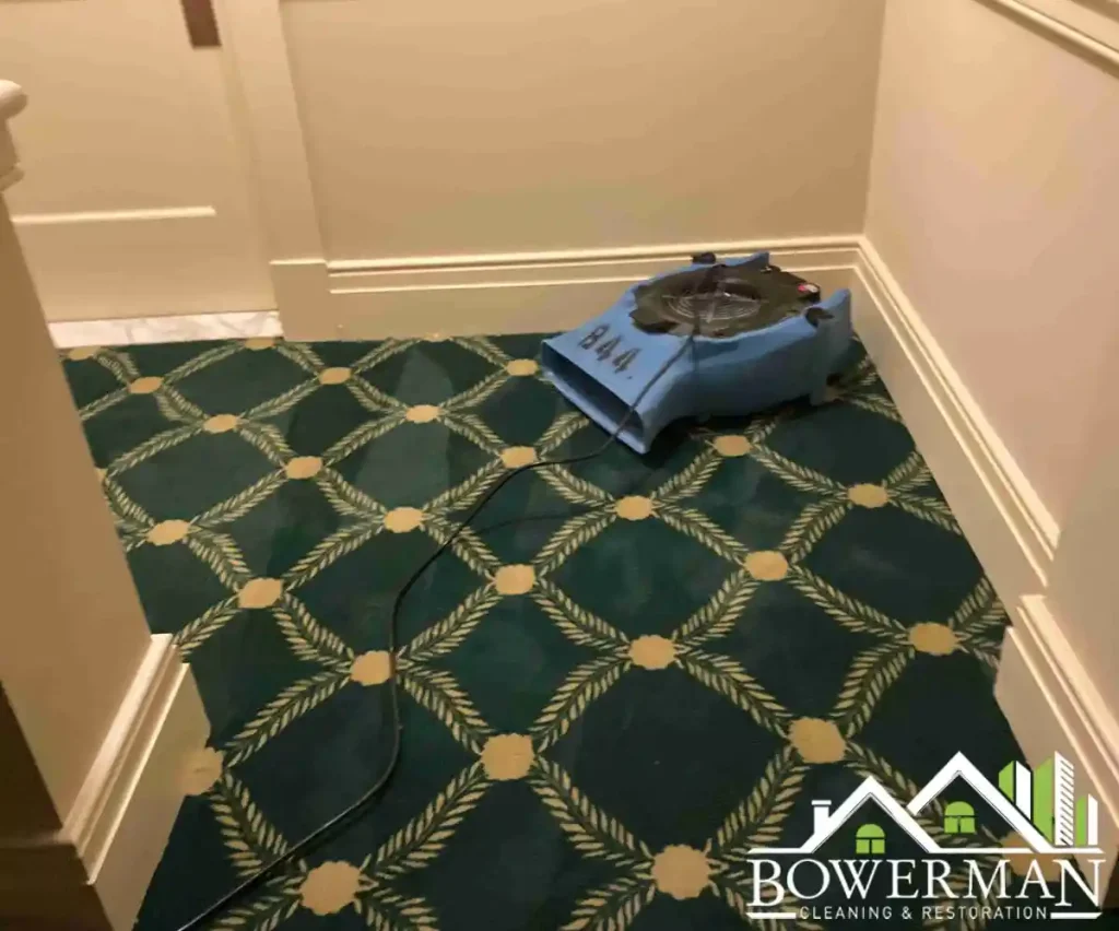 Water damage restoration drying equipment placed on a patterned carpet at a staircase landing with white wainscoting walls
